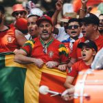 National team supporters in red shirts singing behind a flag
