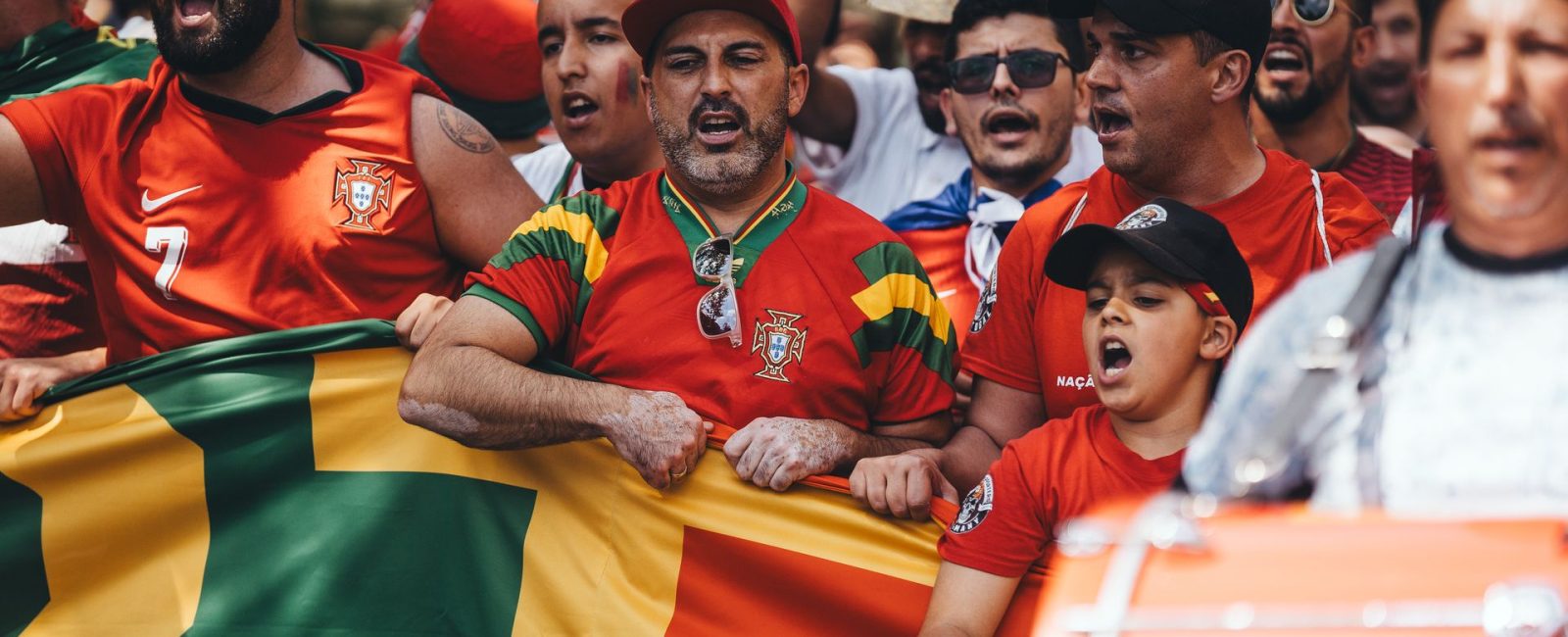 National team supporters in red shirts singing behind a flag