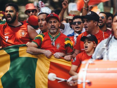 National team supporters in red shirts singing behind a flag