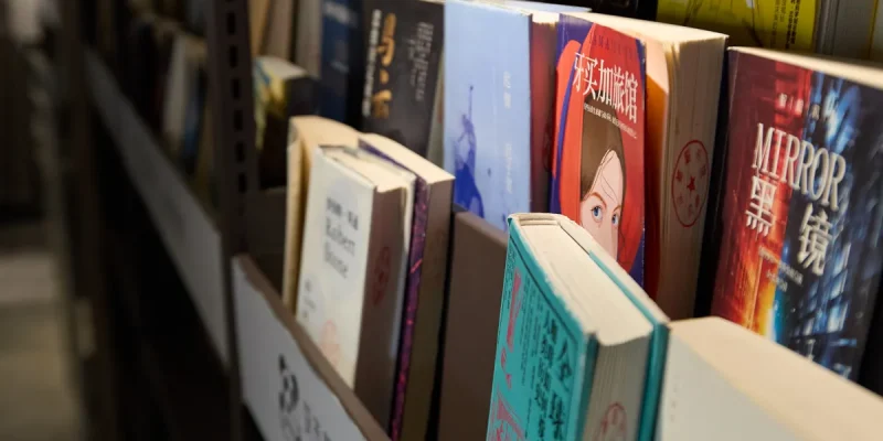 Books neatly arranged on a library shelf, showcasing a variety of genres and languages
