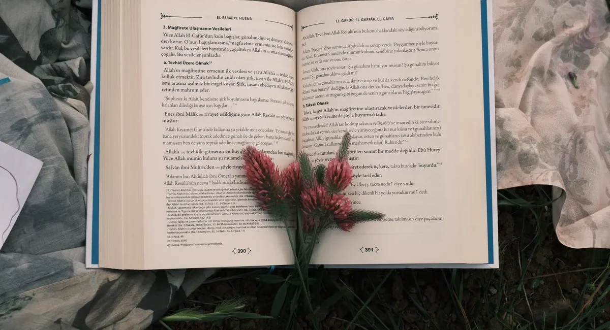 An open book displayed outdoors on floral fabric with red flowers placed on top