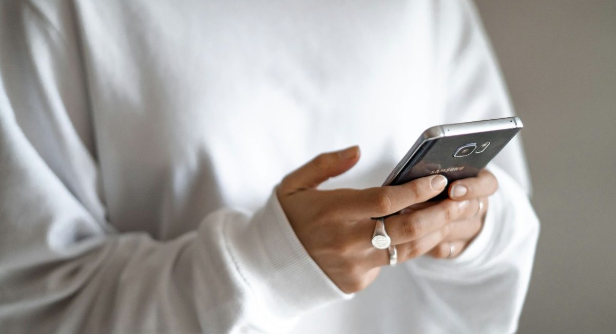 A calmer approach to money: budget first, then plan every repayment: a person in a white jumper checking their household budget on a mobile phone
